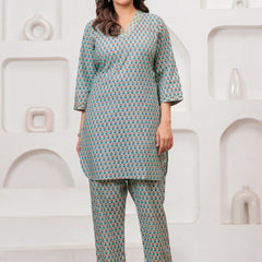 A model wearing a teal green co-ord set featuring a tunic and pants with a red and yellow handblock floral pattern against a white decorative backdrop.