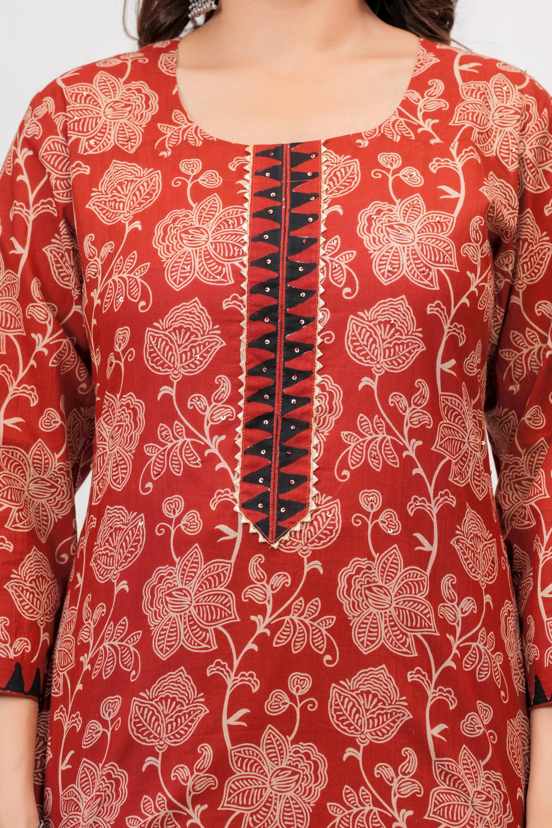 Woman in a Rust Red floral handblock printed cotton kurta set with black and beige geometric patterned dupatta and chevron pants.