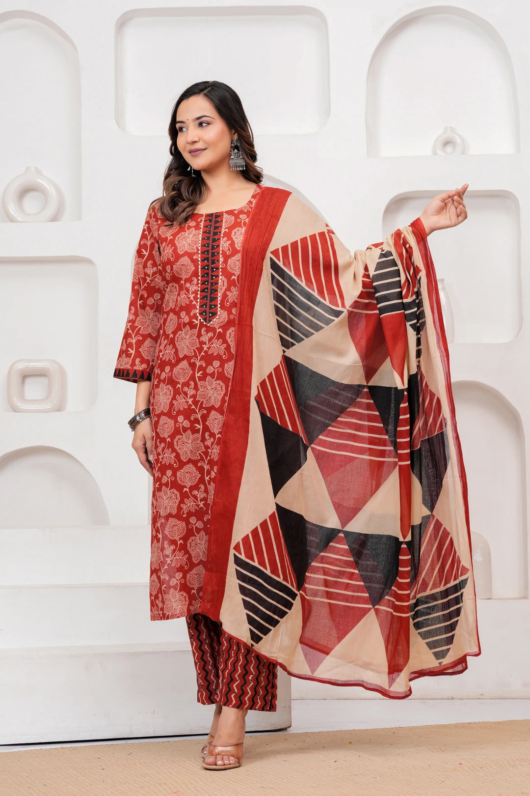 Woman in a Rust Red floral handblock printed cotton kurta set with black and beige geometric patterned dupatta and chevron pants.