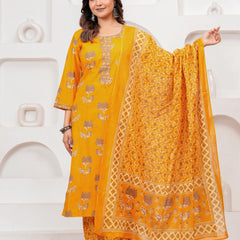 Woman in a mustard yellow floral handblock printed cotton kurta set with a matching dupatta and trousers standing against a minimalist white background.