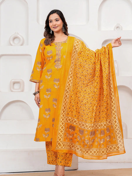 Woman in a mustard yellow floral handblock printed cotton kurta set with a matching dupatta and trousers standing against a minimalist white background.