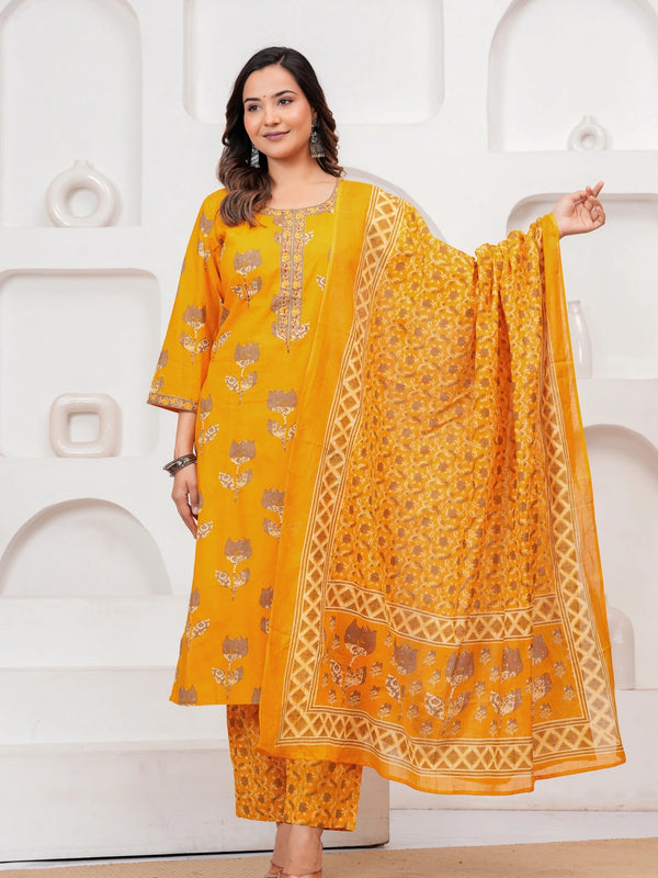 Woman in a mustard yellow floral handblock printed cotton kurta set with a matching dupatta and trousers standing against a minimalist white background.