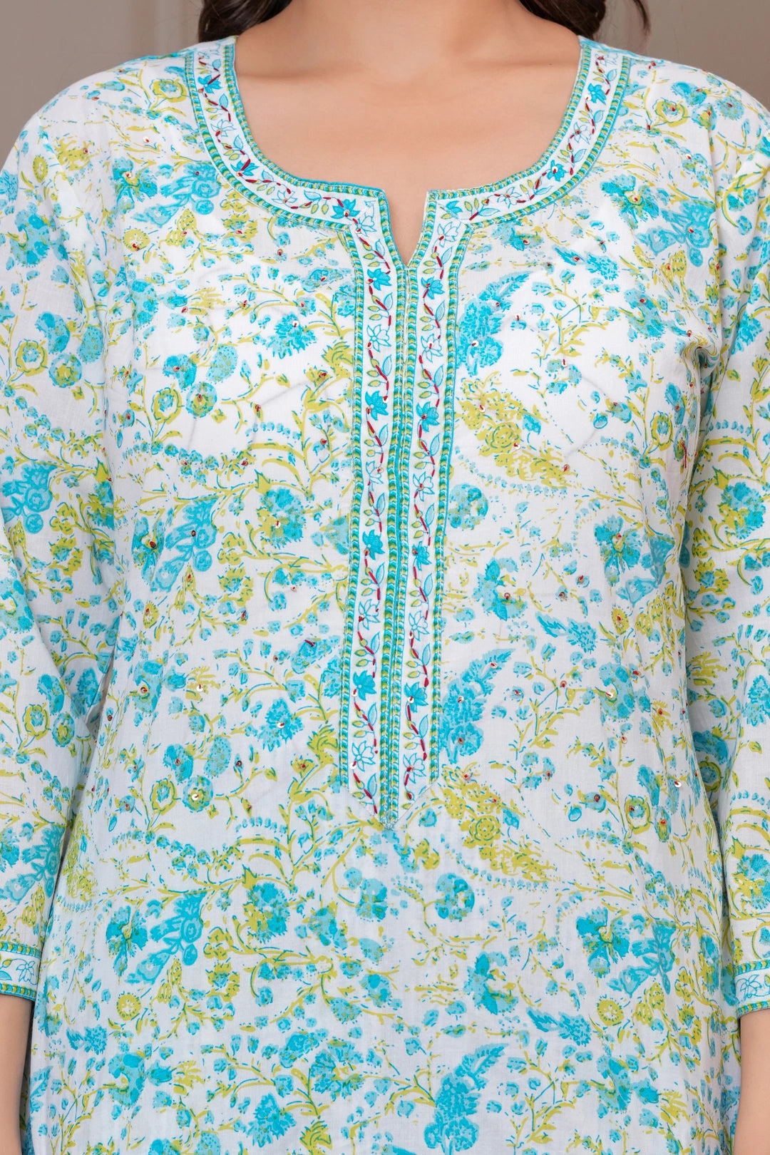 A woman posing in a white cotton kurta set featuring blue and yellow handblock floral prints with a matching dupatta and pants.