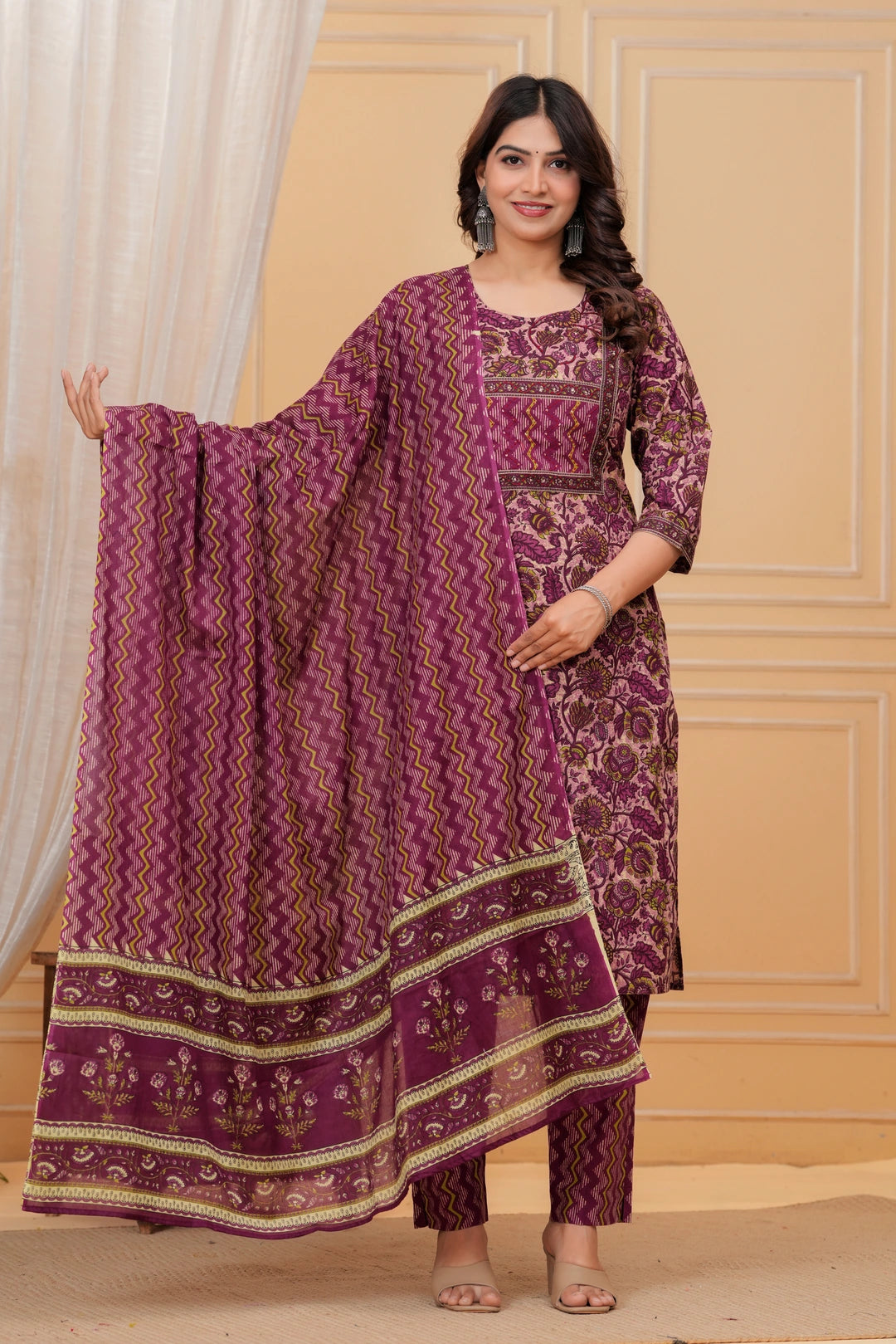 Woman wearing a purple handblock printed cotton kurta set with a chevron pattern dupatta and matching straight pants in a studio setting.