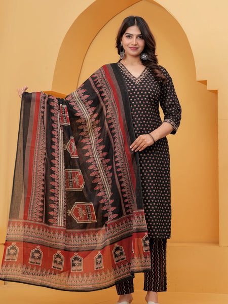 Model posing in a black handblock printed cotton kurta set with a large floral motif dupatta and zigzag print pants against a traditional yellow arch background.
