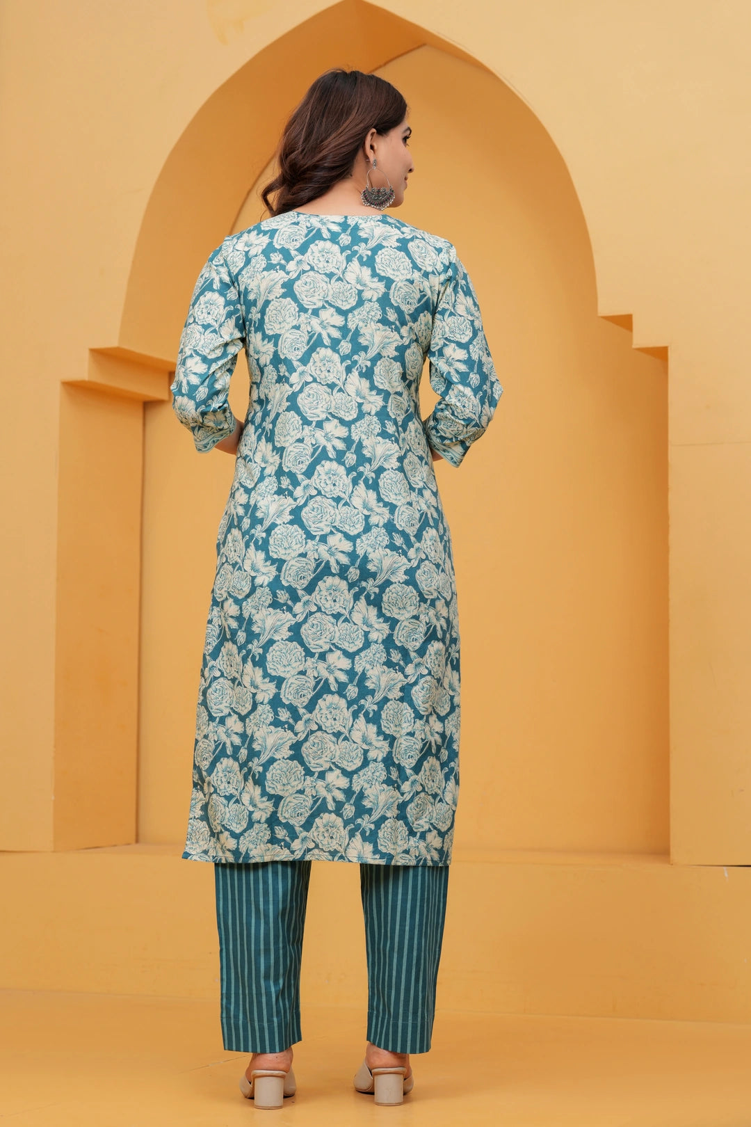 A woman wearing a teal blue cotton kurta with off-white floral handblock prints and teal vertical striped pants.
