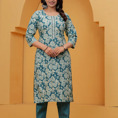A woman wearing a teal blue cotton kurta with off-white floral handblock prints and teal vertical striped pants.