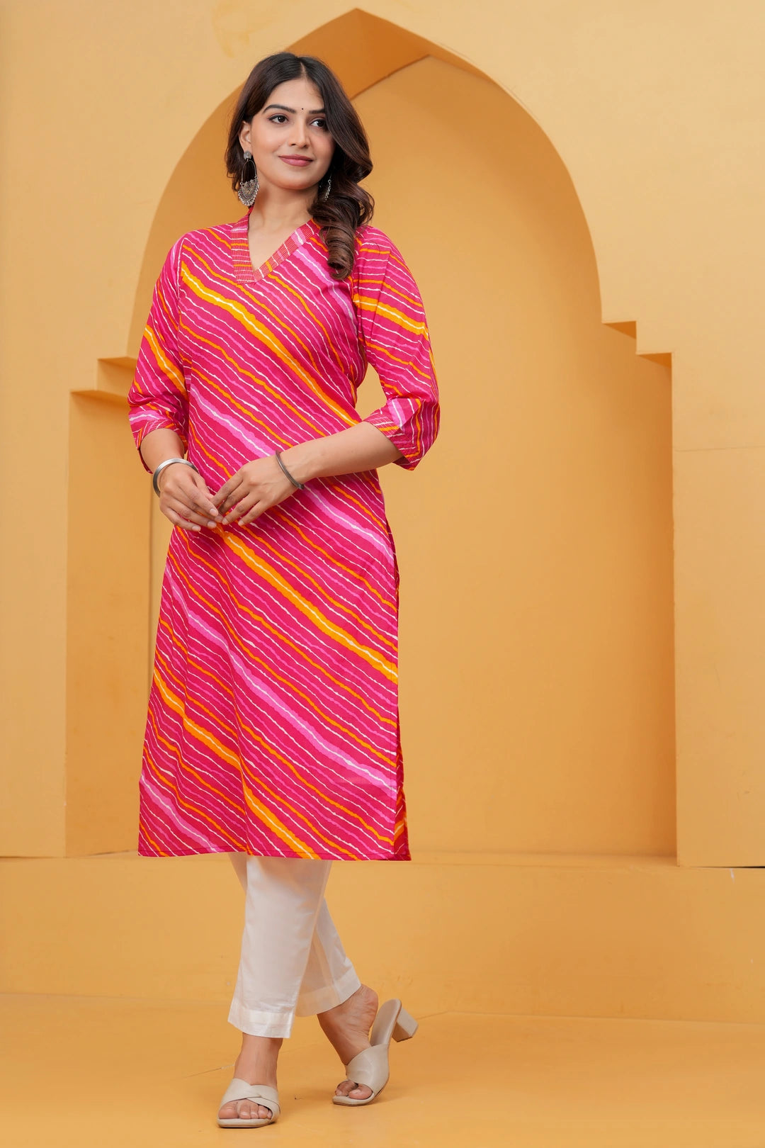 Woman wearing a bright pink Leheriya printed cotton kurta with orange and white stripes, featuring a V-neck and three-quarter sleeves.