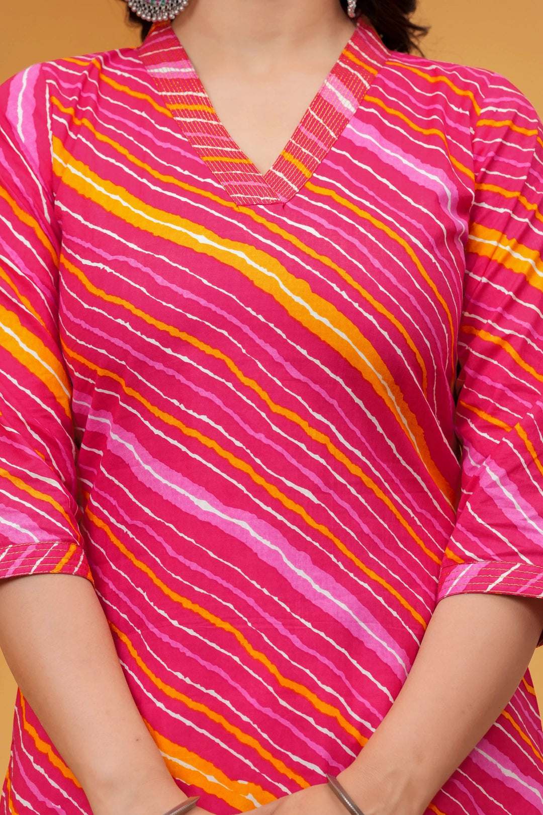 Woman wearing a bright pink Leheriya printed cotton kurta with orange and white stripes, featuring a V-neck and three-quarter sleeves.