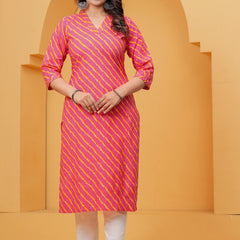 A woman posing in a pink and yellow Leheriya diagonal striped cotton kurta with white straight-cut trousers against a yellow architectural background.